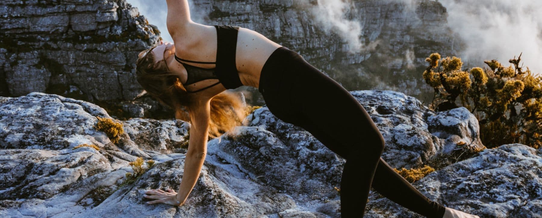 Woman in a backbend stretch on a rocky mountainside